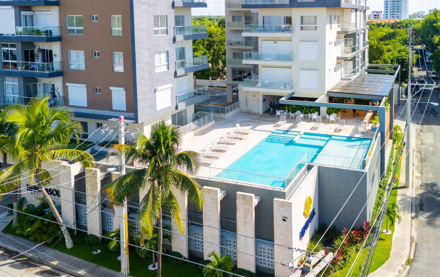 A modern building with a rooftop swimming pool, multiple balconies, and lush greenery.