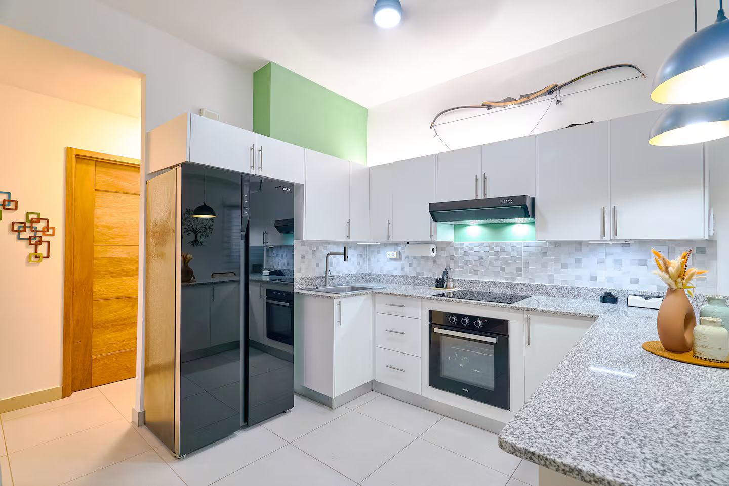 A modern kitchen with white cabinets, a black refrigerator, a built-in oven, and a granite countertop.