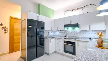 A modern kitchen with white cabinets, a black refrigerator, a built-in oven, and a granite countertop.