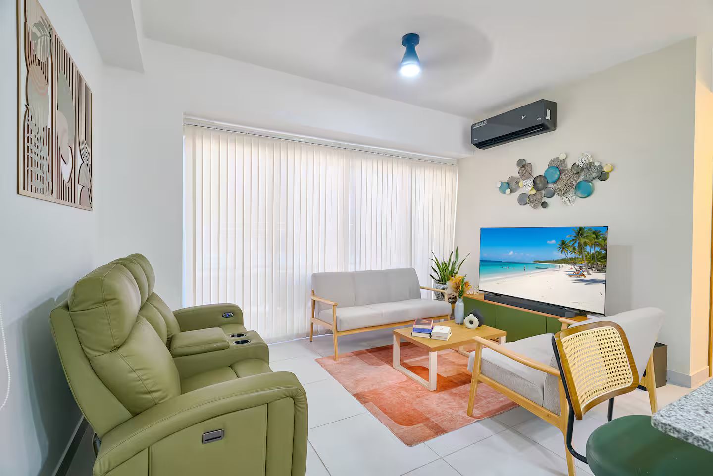 A living room with a sofa, a green armchair, a coffee table, and a TV displaying a beach scene.
