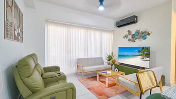 A living room with a sofa, a green armchair, a coffee table, and a TV displaying a beach scene.