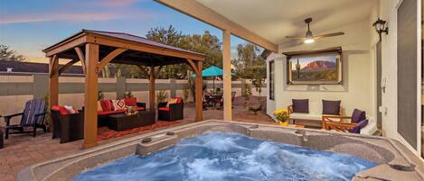 A hot tub area with a pergola, seating, and a view of a mountain through a window.