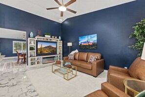 Un salon moderne avec un téléviseur, un canapé en cuir et un ventilateur de plafond.