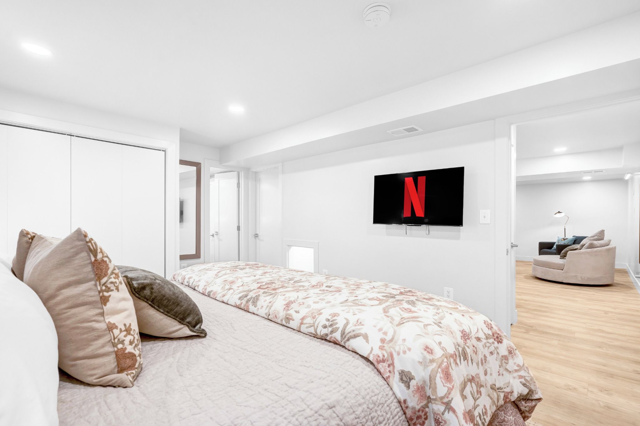 A modern bedroom with a large bed, a flat-screen TV mounted on the wall, and a walk-in closet.