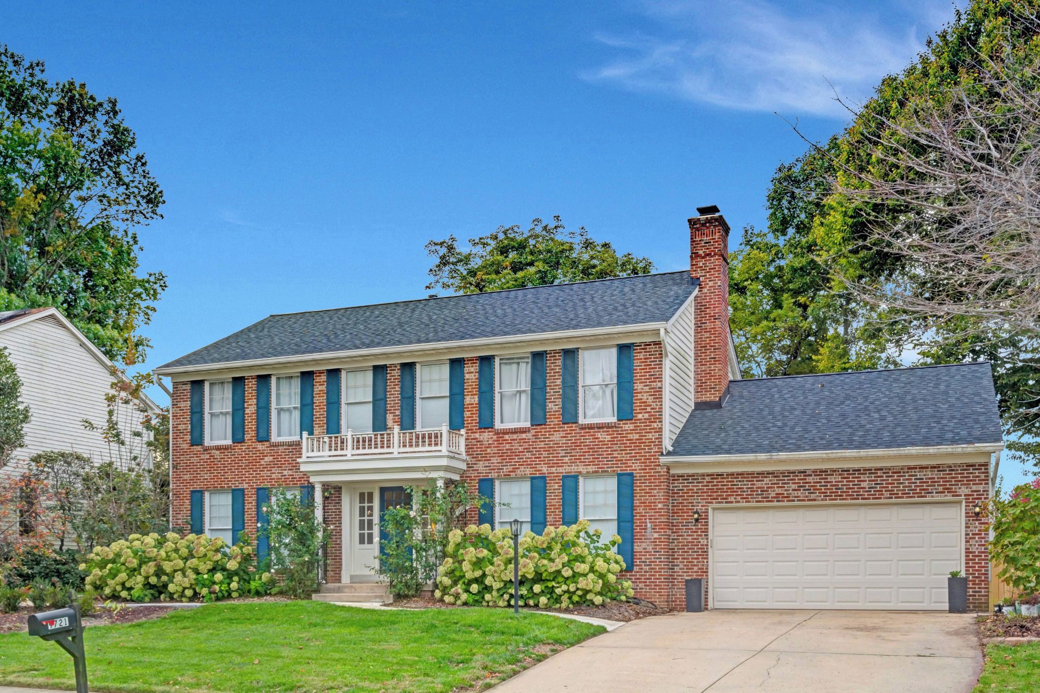 A two-story brick house with a front porch, a garage, and a well-maintained lawn.