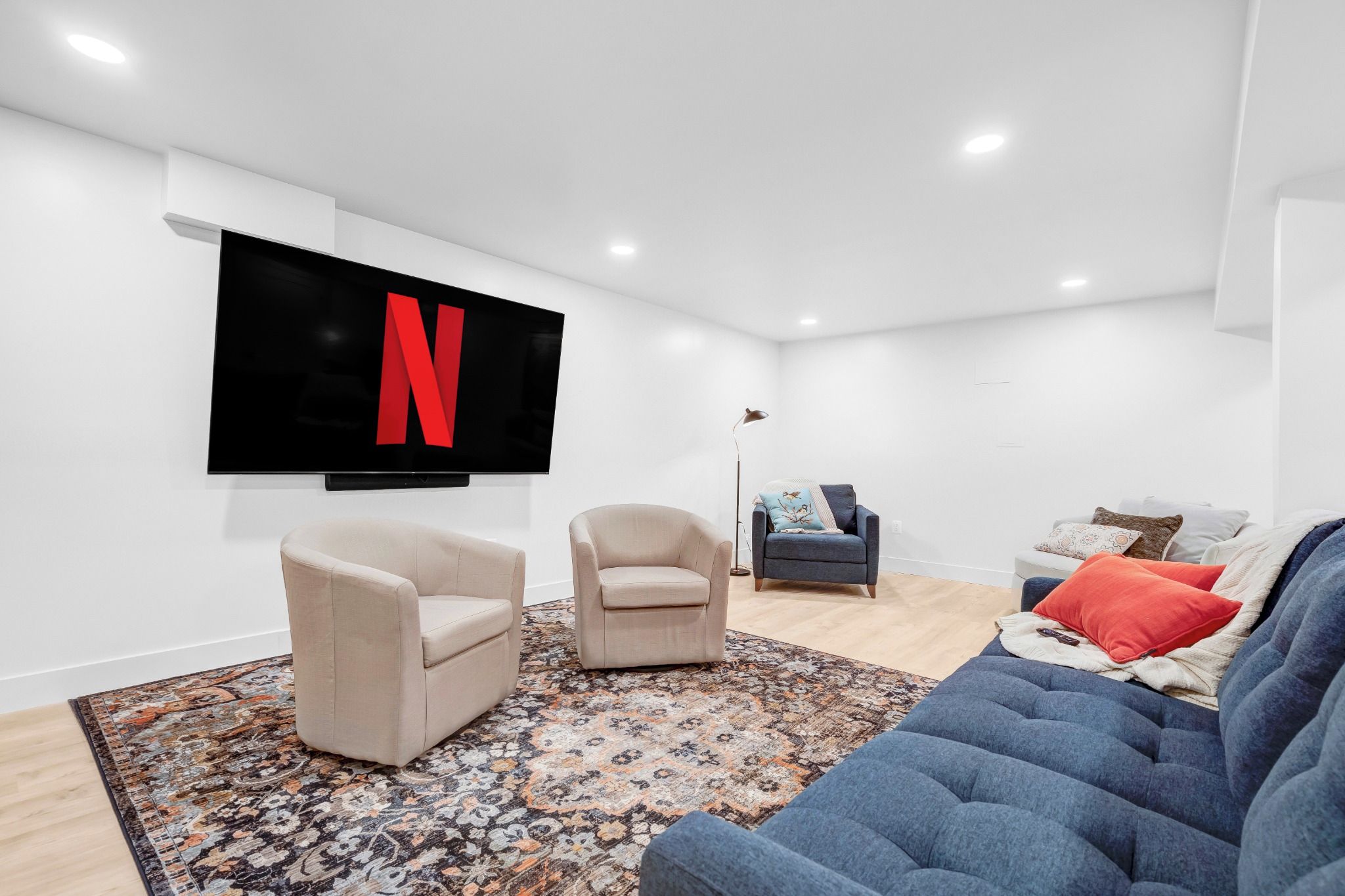A modern living room with a flat-screen TV displaying the Netflix logo, two armchairs, a sofa, and a patterned rug.