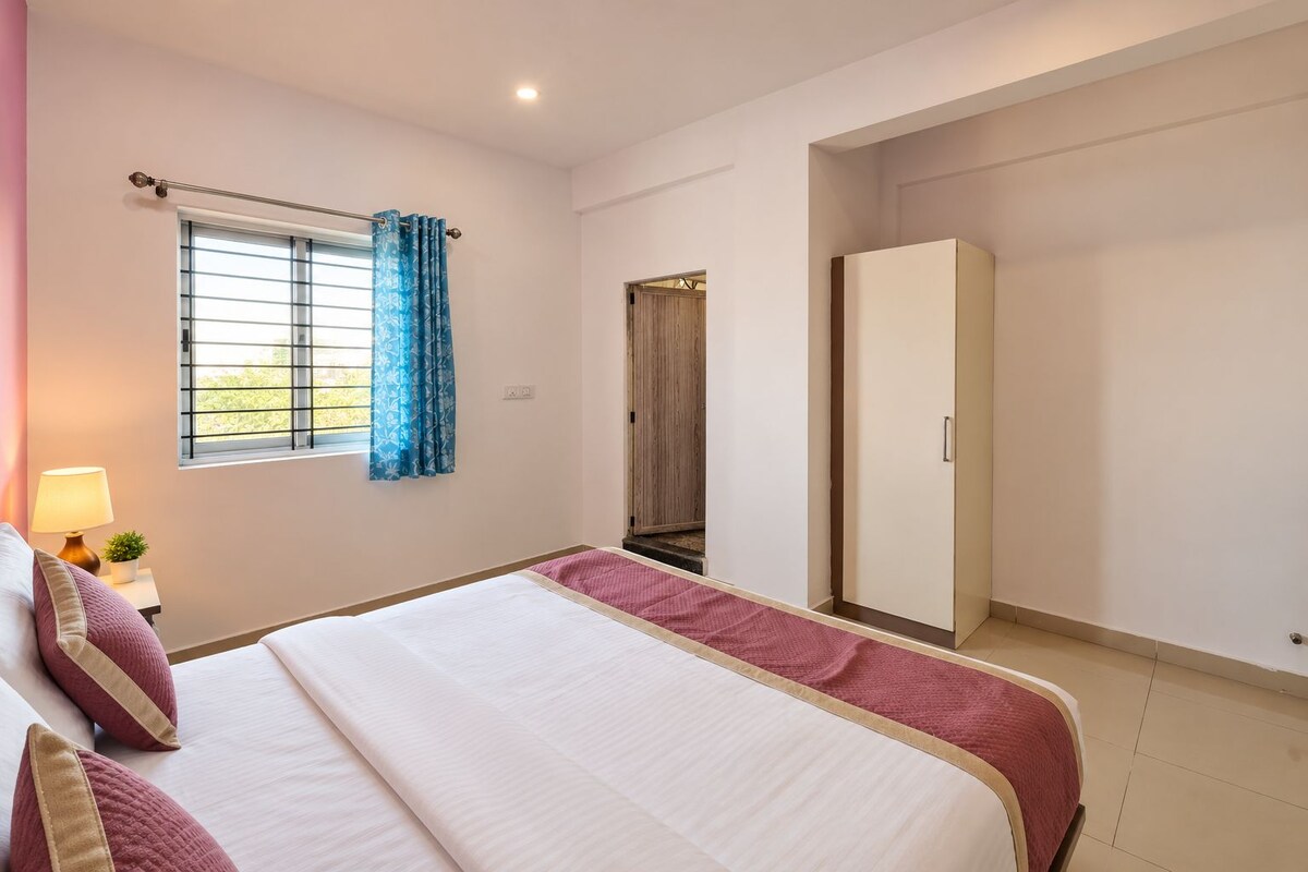 Un dormitorio con cama, armario, ventana con cortinas y una lámpara de noche.