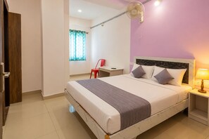 Una habitación de hotel con cama, mesita de noche y ventana con cortinas.
