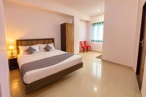 Ein Hotelzimmer mit einem großen Bett, einem Nachttisch, einem Kleiderschrank, einem Fenster mit Vorhängen und zwei roten Stühlen.