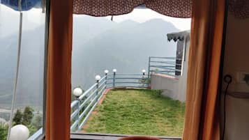 Vista desde una ventana con balcón, sobre un área verde y montañas distantes.