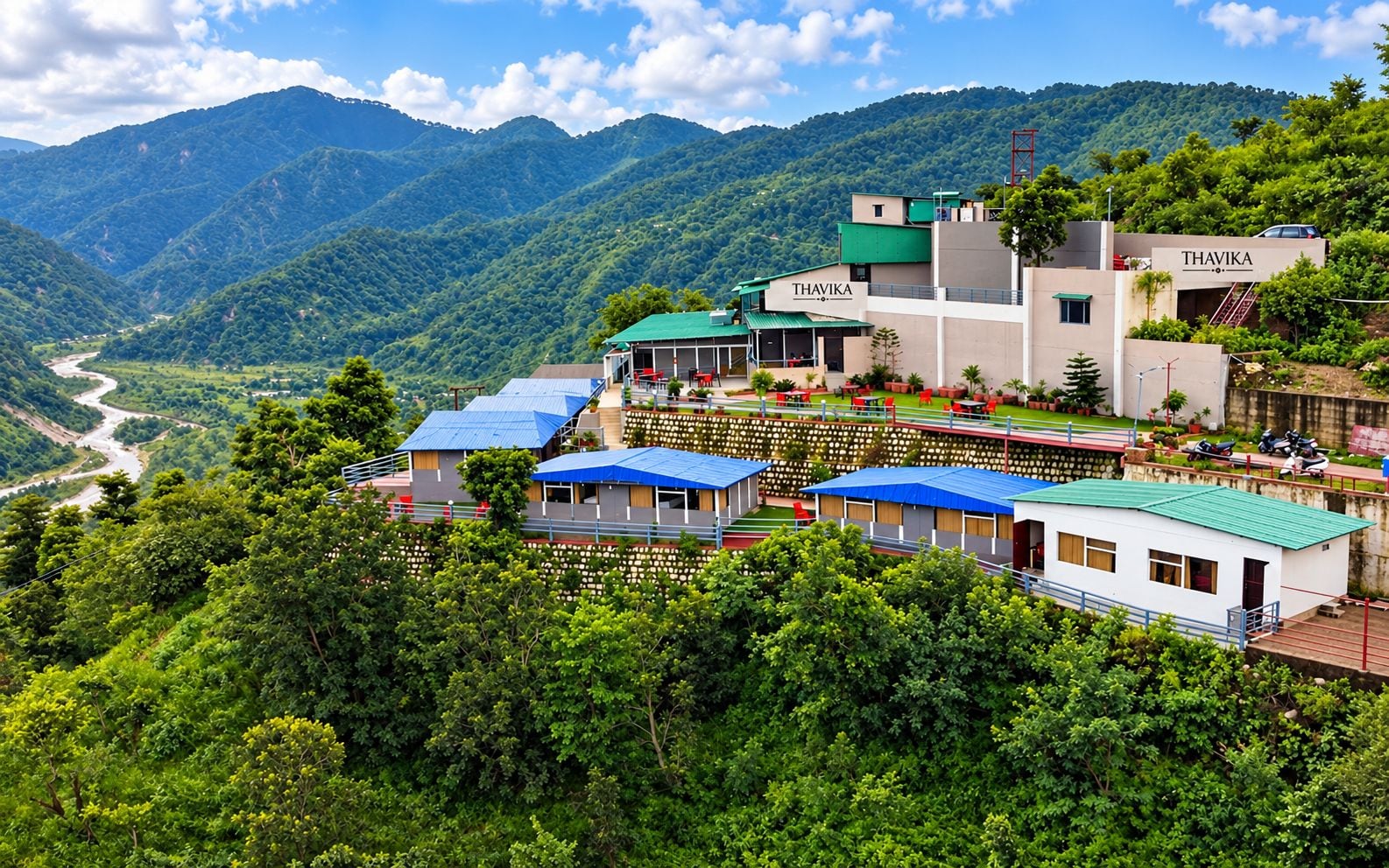 Un hotel su una collina con diversi edifici, un fiume sullo sfondo e vegetazione rigogliosa.