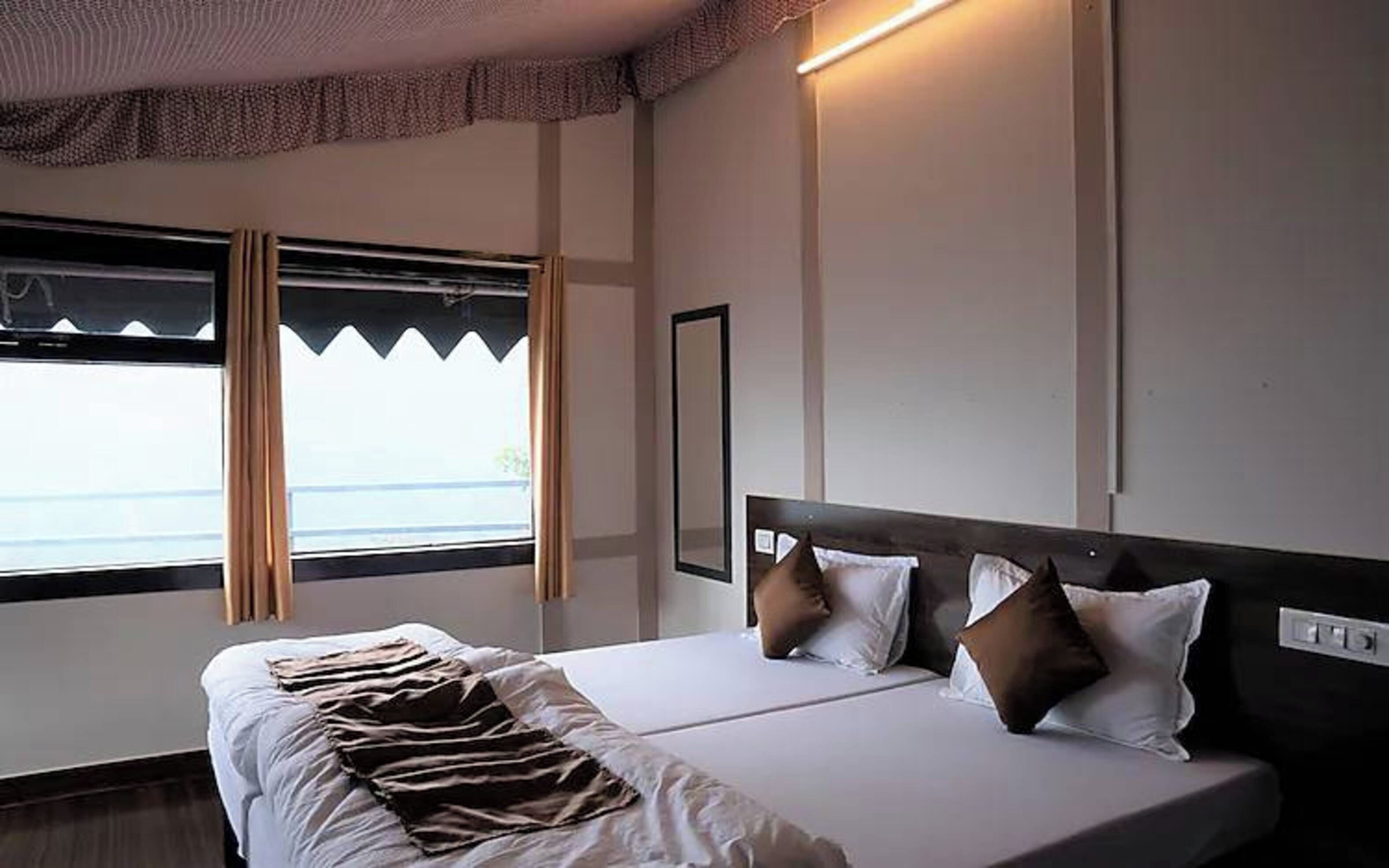 Habitación de hotel con cama, ventana con cortinas, lámpara de pared y espejo.