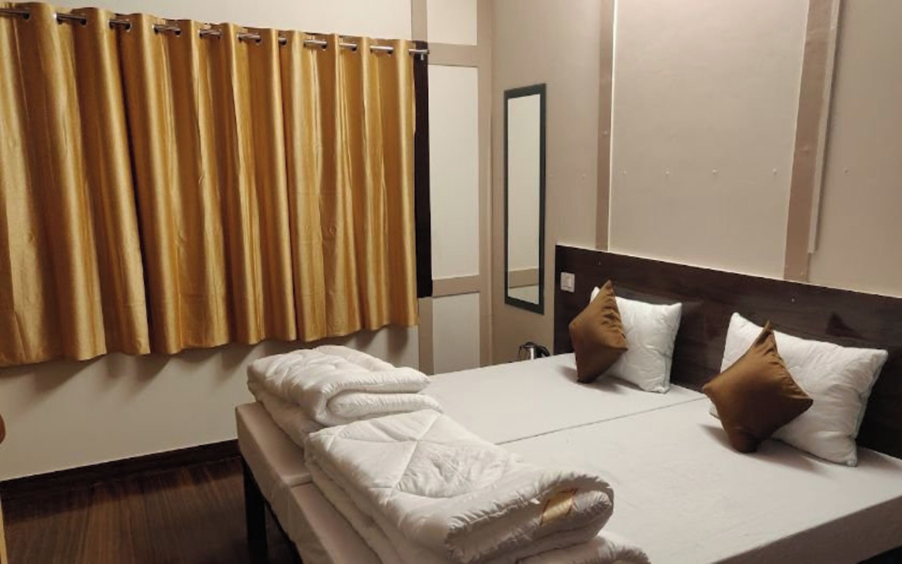A hotel room with a bed, a bedside table, a mirror, and a window with curtains.