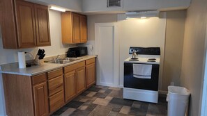 A compact kitchen with wooden cabinets, a stainless steel sink, a microwave, and a white stove.