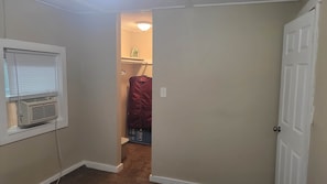 Un pasillo estrecho con una puerta blanca a la derecha, una pared blanca con una ventana a la izquierda y una chaqueta roja colgada en la pared.