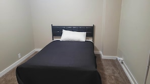 A small, single-bed room with a dark headboard and a white pillow.