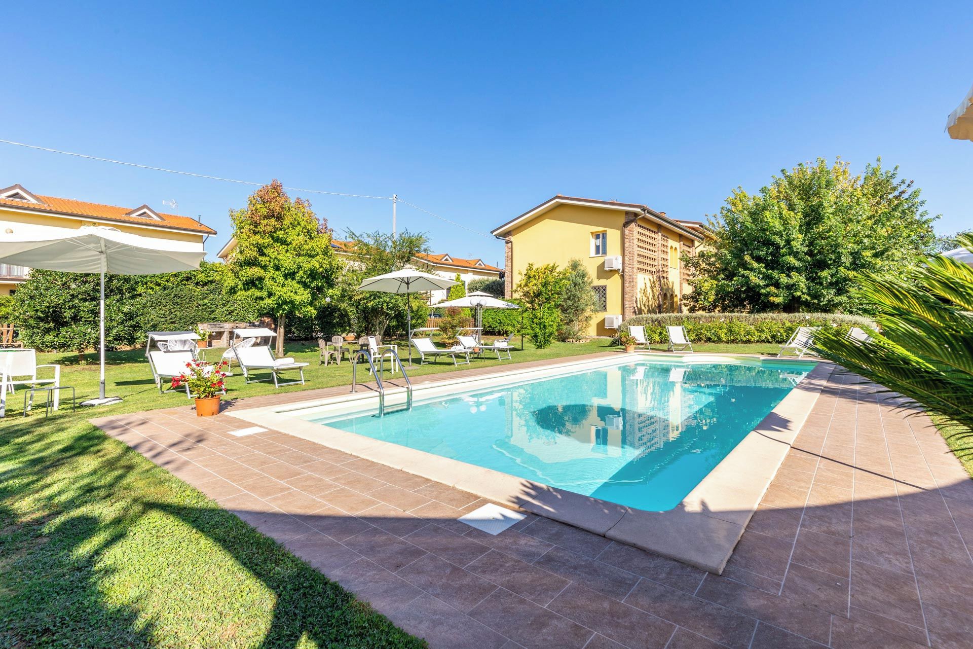 A swimming pool with lounge chairs and umbrellas, surrounded by a well-maintained lawn and trees.