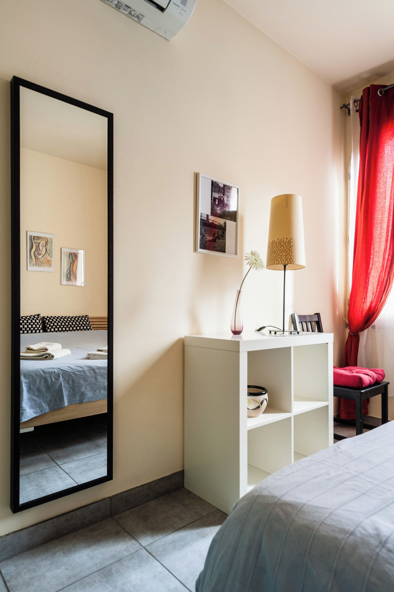 A hotel room with a bed, a bedside table with a lamp, a mirror, and artwork on the wall.