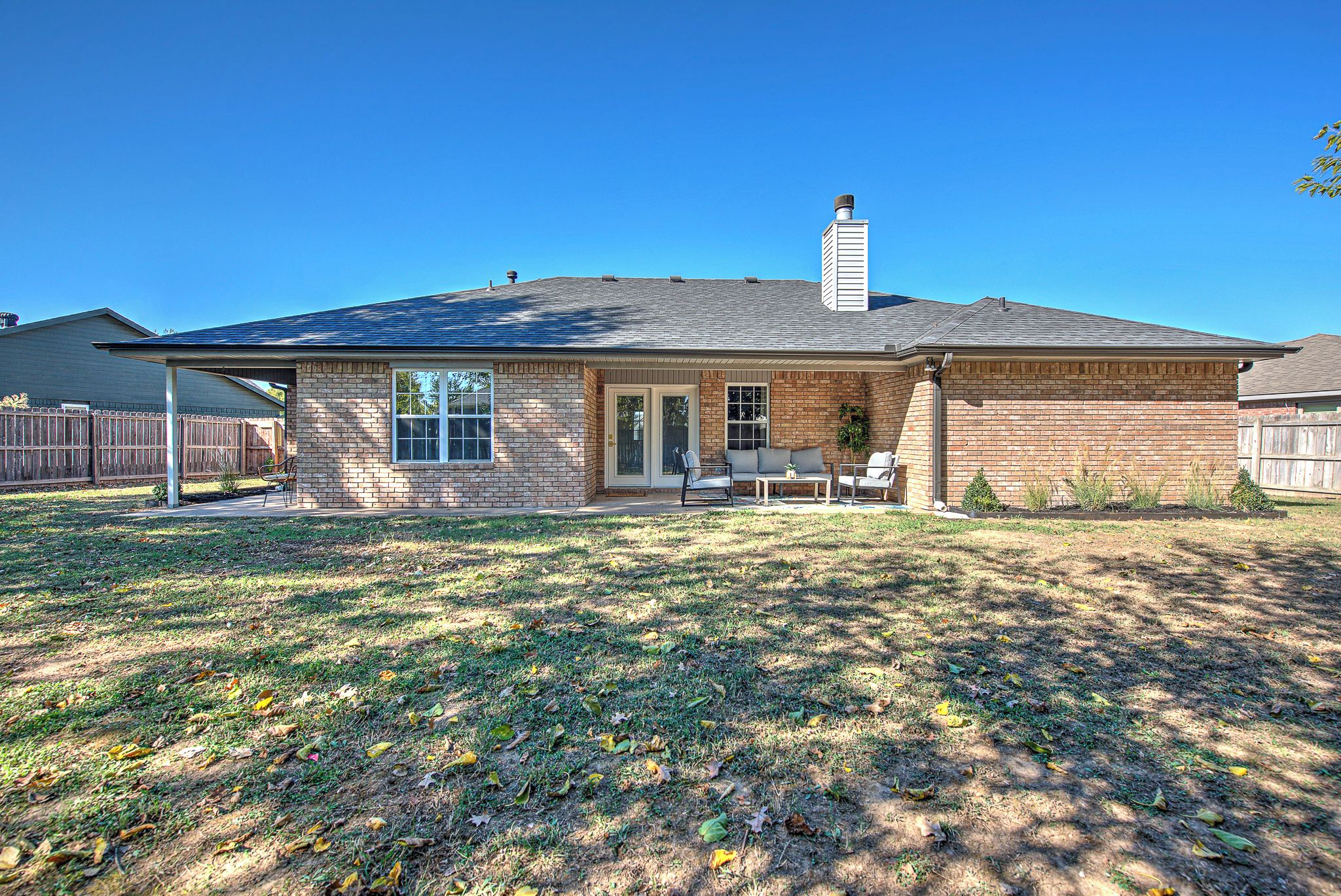 A single-story house with a covered patio, a brick exterior, and a fenced backyard.