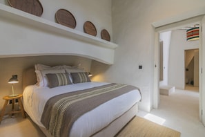 A bedroom with a large bed, bedside lamps, and a wall-mounted shelf with decorative items.