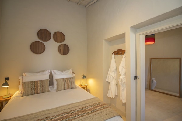 Un dormitorio con una cama, dos lámparas de noche, un espejo en la pared y una puerta que da a un baño.