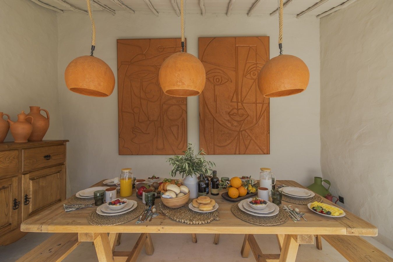 Un tavolo da pranzo in legno con diversi cibi e bevande, un vaso con fiori e due quadri astratti appesi al muro.