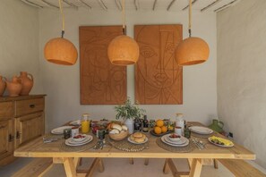 Una mesa de madera con diversos alimentos y bebidas, un florero con flores y dos cuadros abstractos en la pared.