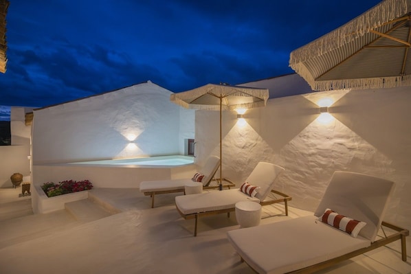 A modern outdoor relaxation area with a hot tub, lounge chairs, and ambient lighting.