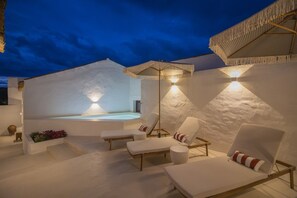 Un área moderna para relajarse al aire libre con un jacuzzi, sillones de descanso e iluminación ambiental.