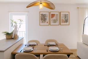 Comedor con una mesa de madera dispuesta para cuatro, sillas, lámpara colgante y cuadros en la pared.