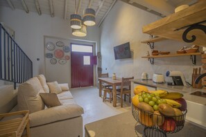 Ein geräumiger Wohnbereich mit einer Couch, einem Esstisch und einer Obstschale. Eine Treppe und eine Tür zu einem anderen Raum sind sichtbar.