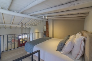 Un dormitorio con una cama grande, una pared de ladrillo y un balcón con barandilla.