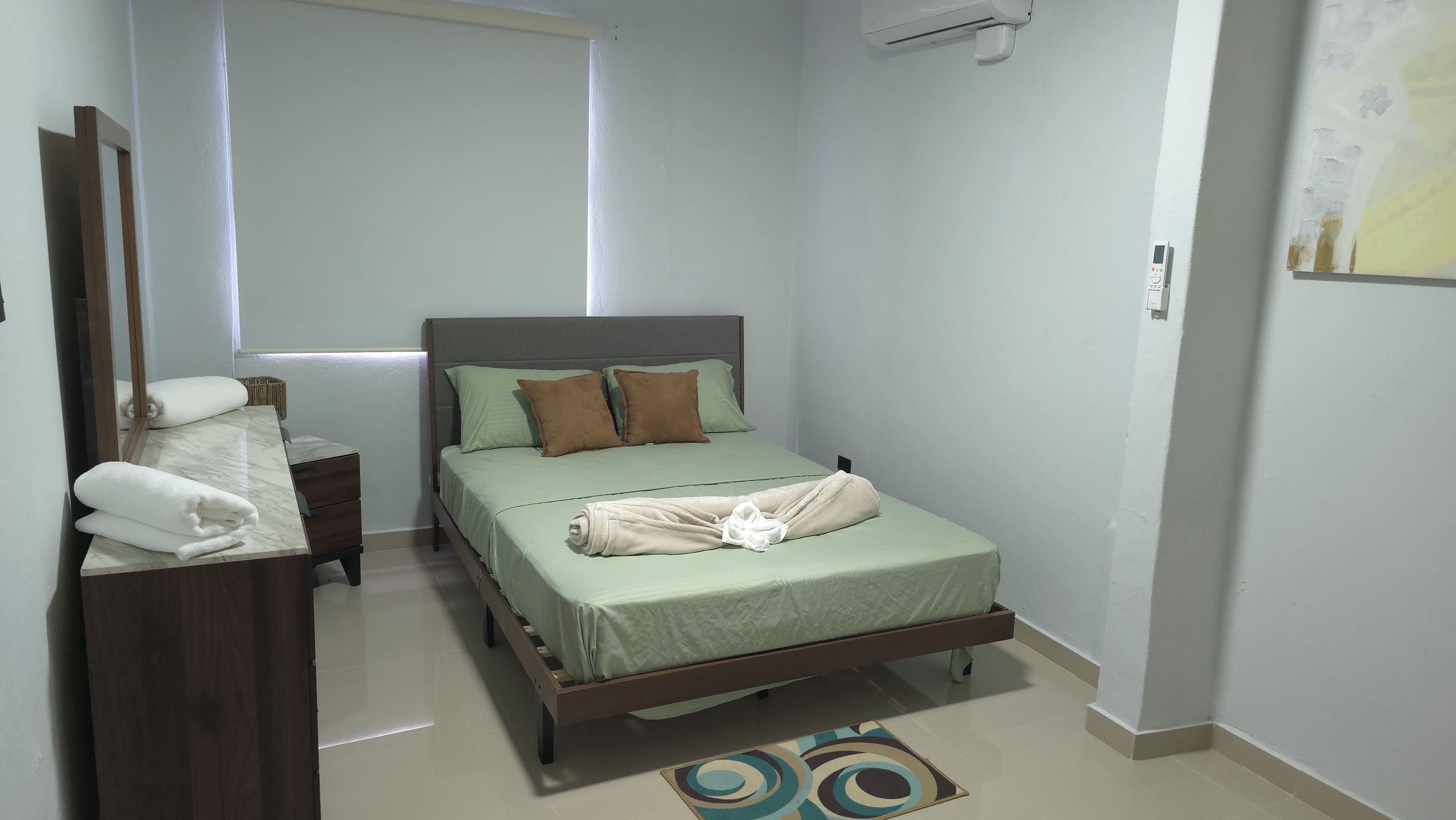 A bedroom with a bed, a bedside table, a mirror, and a wall-mounted air conditioner.