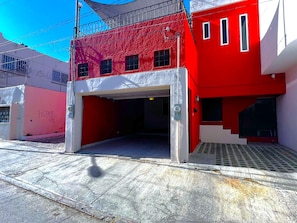 Un edificio rojo con una puerta de garaje blanca, una escalera metálica y una cámara de seguridad.