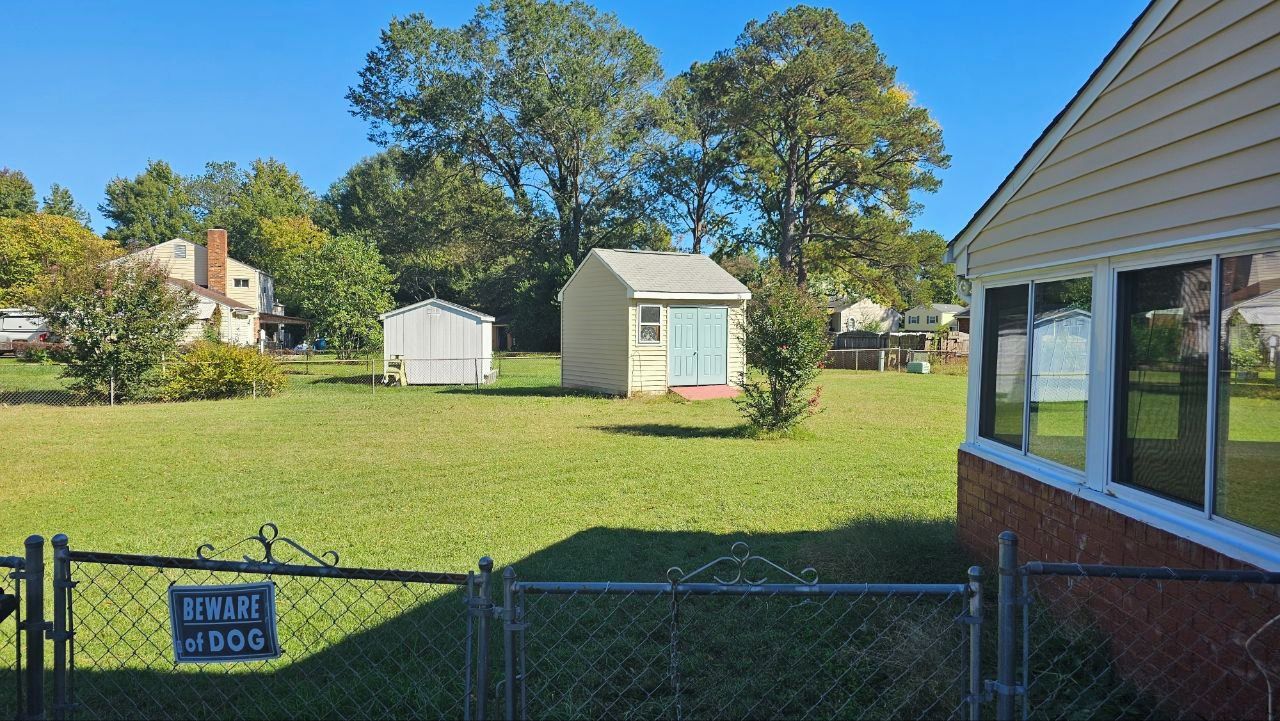 A fenced yard with a 'BEWARE OF DOG' sign, a small shed, and a house with a garage.