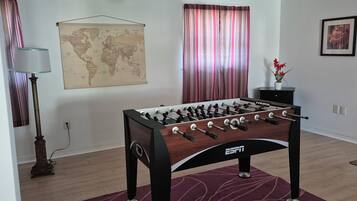 A foosball table in a room with a world map on the wall, a lamp, and a framed picture.