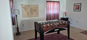 Una mesa de fútbolín en una habitación con un mapa del mundo en la pared, una lámpara y un cuadro enmarcado.