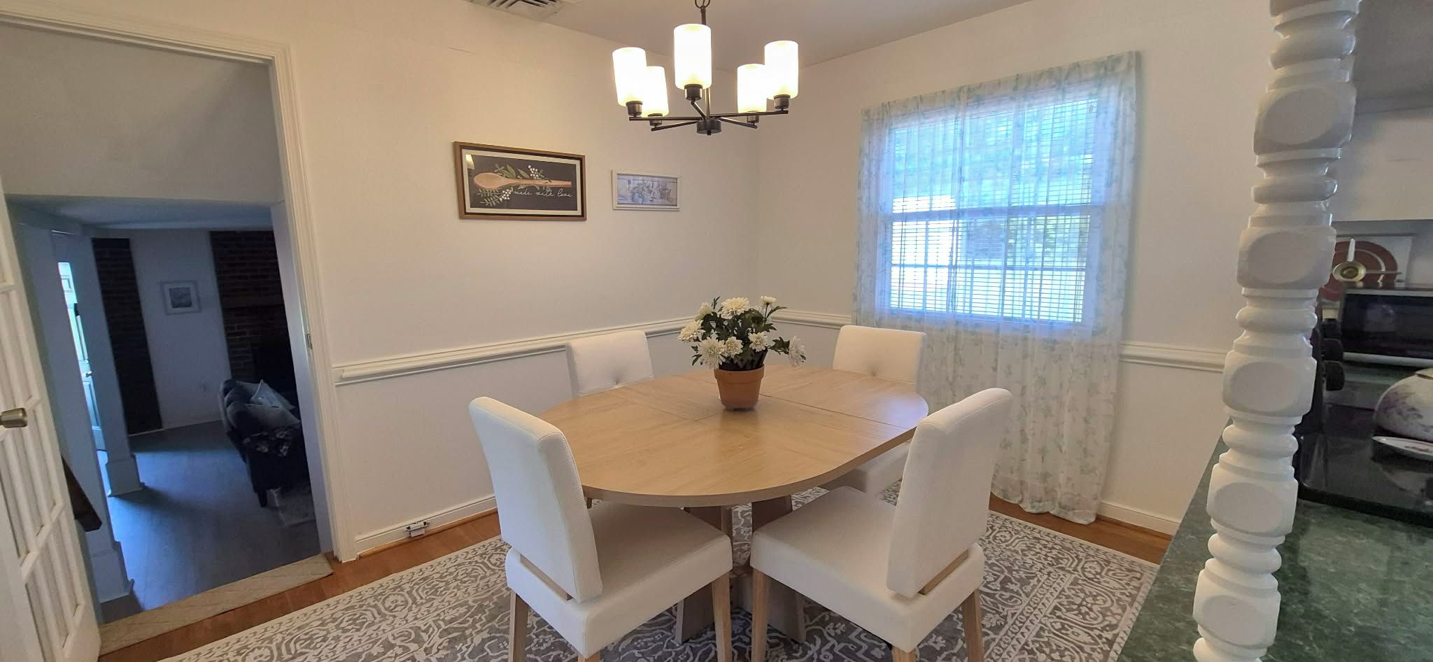 Una sala da pranzo con un tavolo rotondo, sedie bianche, un lampadario e una finestra con tende.