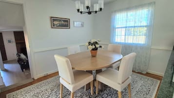 A dining area with a round table, four chairs, a chandelier, and a window with curtains.