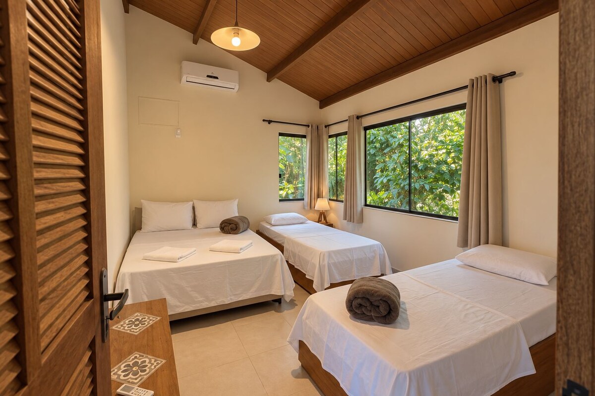 Une chambre d’hôtel avec deux lits simples, un plafond en bois, un appareil de climatisation et une fenêtre avec des rideaux.