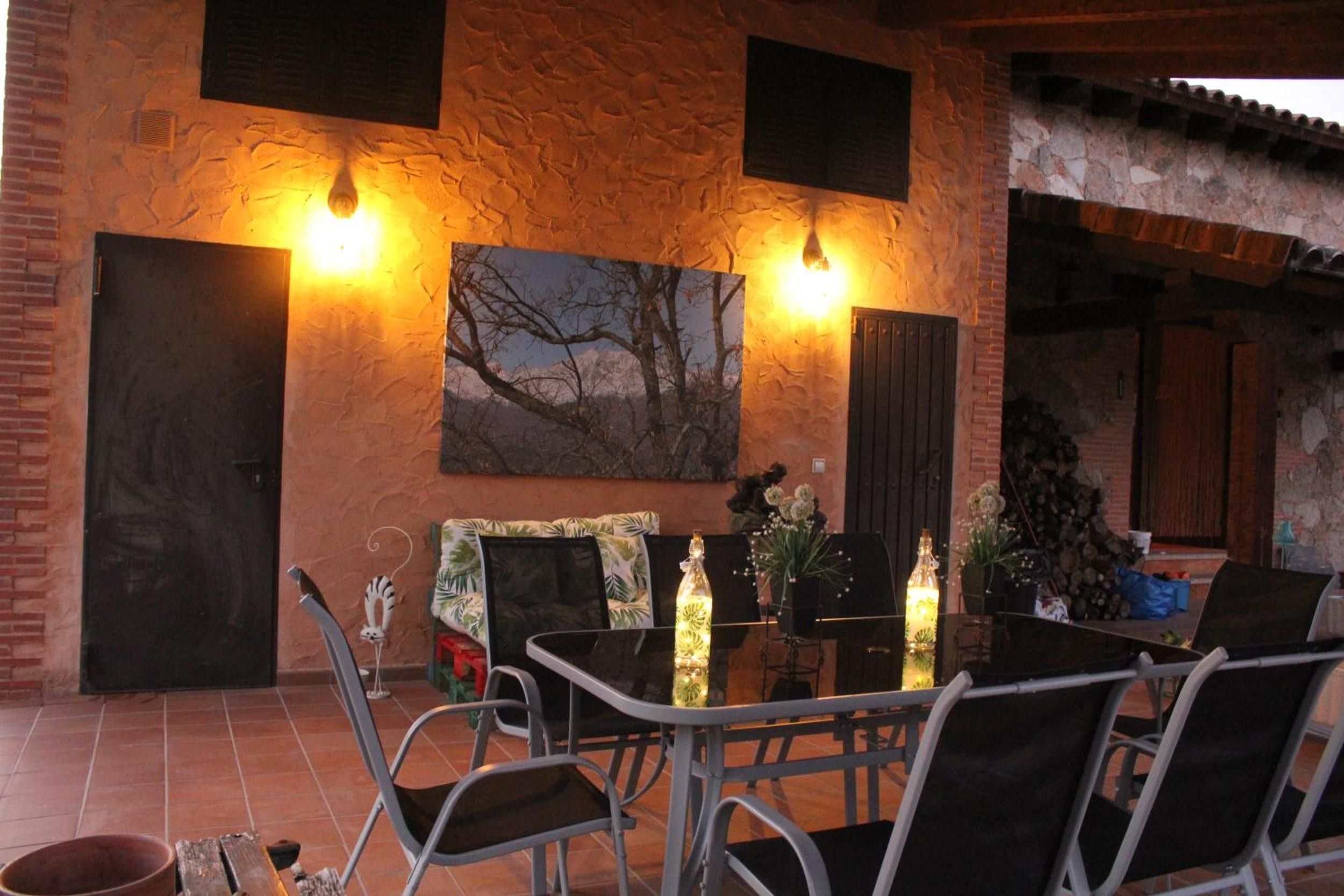 Un patio al aire libre con paredes de ladrillo, una mesa con sillas y dos luces fijadas a la pared.