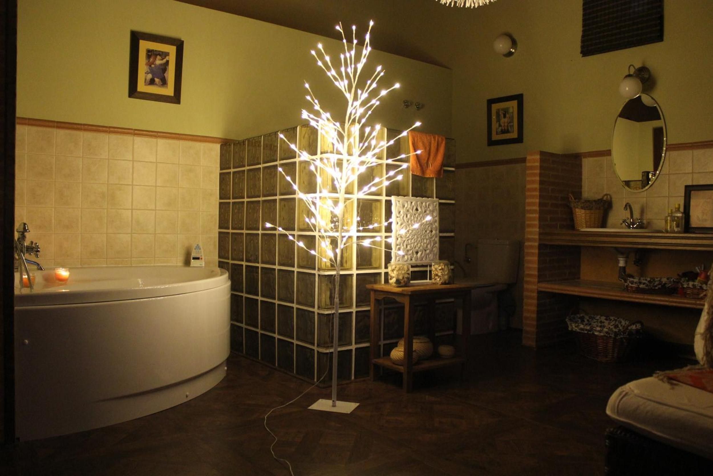 Ein Badezimmer mit einer Badewanne, einer Duschkabine, einem Waschbecken und einem Spiegel. Im Duschbereich befindet sich ein dekorativer Baum mit Lichterketten.
