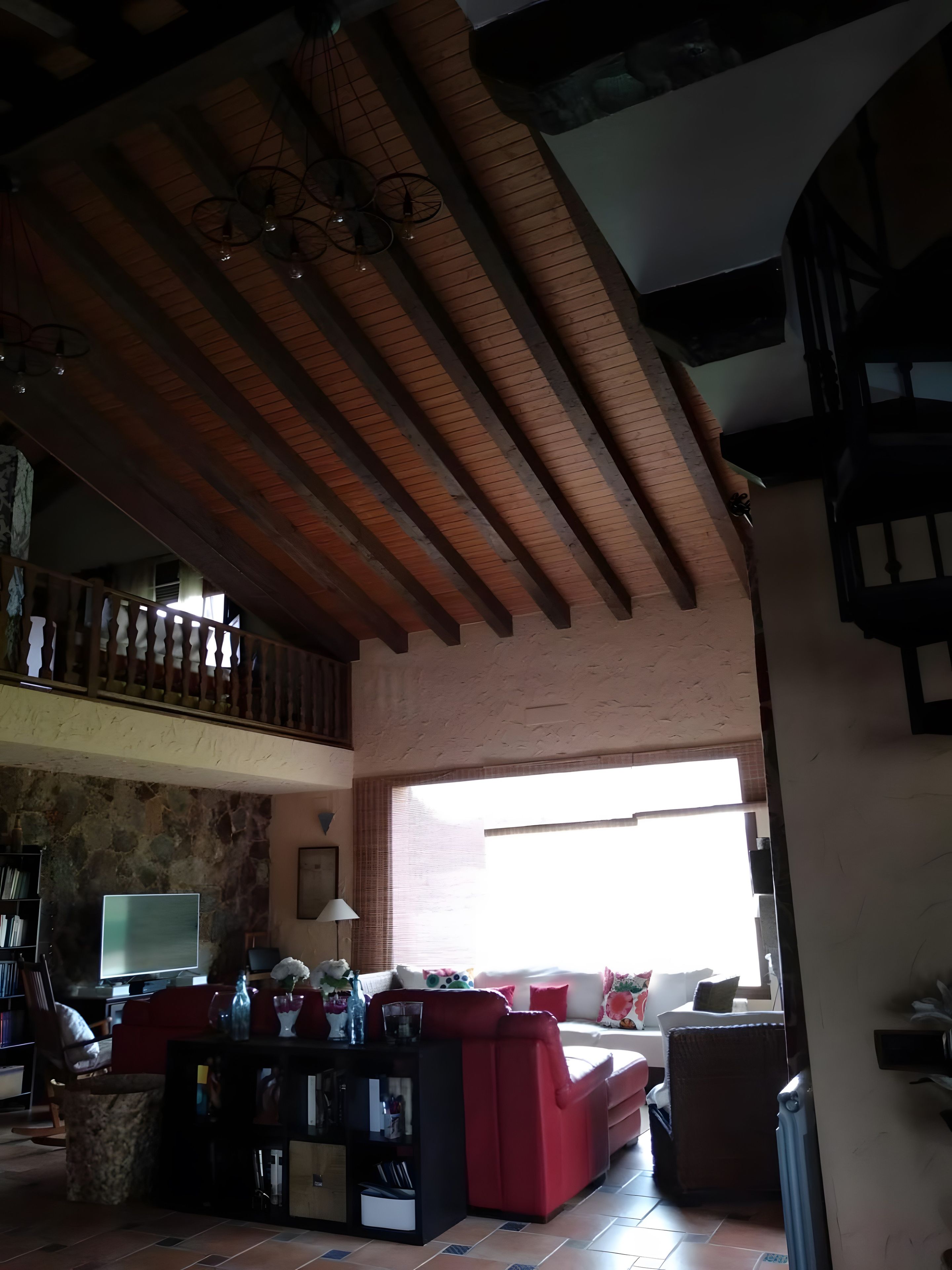 Amplia sala de estar con techo alto, sofá rojo, televisor y pared de piedra.