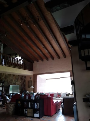 A spacious living area with a high ceiling, a red sofa set, a television, and a stone wall.
