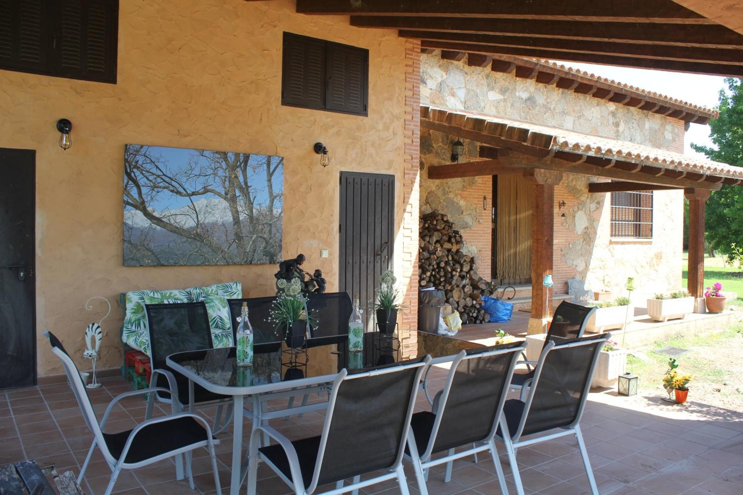 Un patio al aire libre con una mesa y sillas de vidrio, un cuadro en la pared y una zona cubierta con techo de madera.