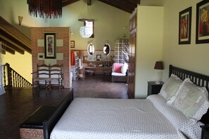 A bedroom with a large bed, a wooden chair, a dresser, a mirror, and a hanging light fixture.