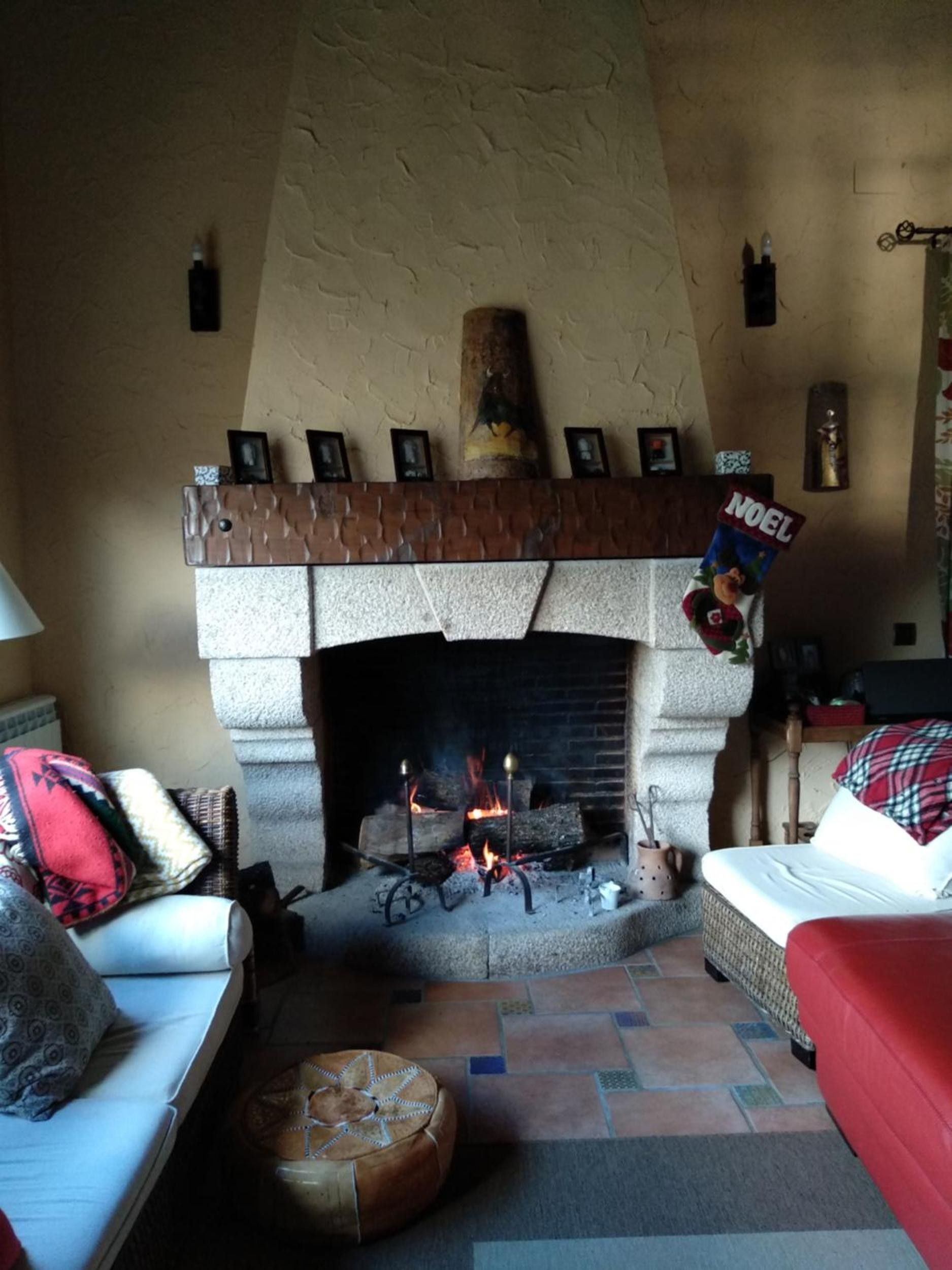 Una sala de estar acogedora con chimenea de piedra, un sofá, un sillón rojo y un letrero decorativo que dice 'NOEL'.