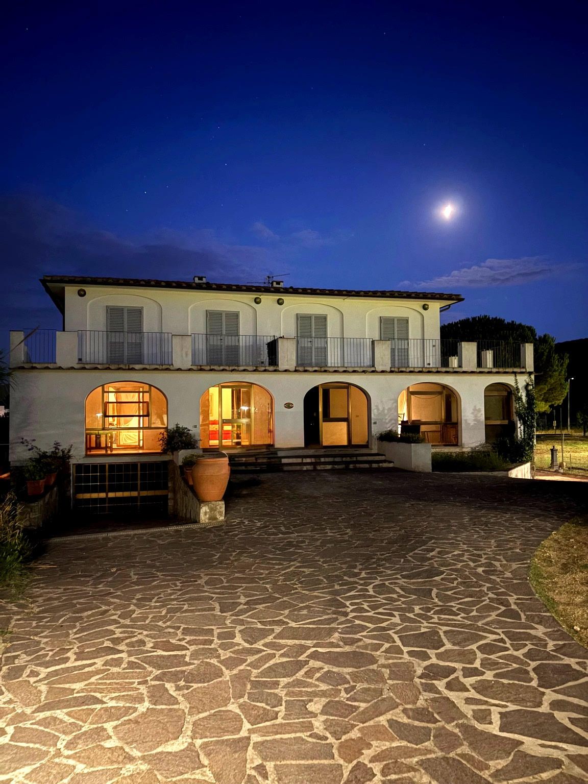 A two-story building with a stone-paved courtyard, multiple arched doorways, and a balcony with railings.