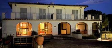 A two-story building with a stone-paved courtyard, multiple arched doorways, and a balcony with railings.