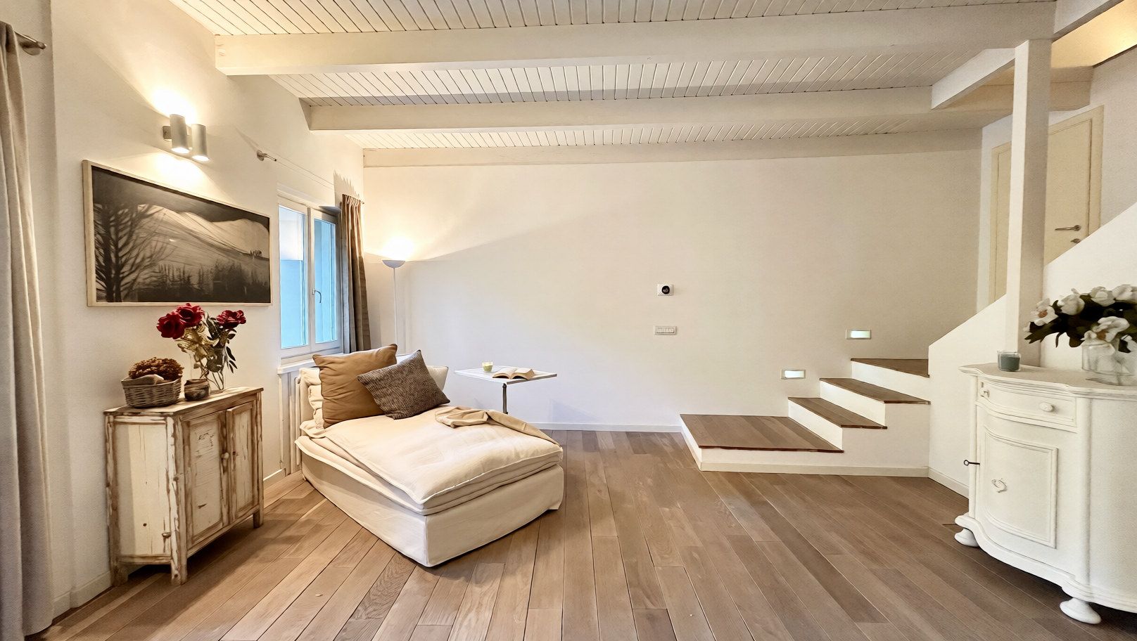 A bedroom with a bed, a nightstand, a dresser, a staircase, and a painting on the wall.